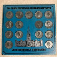 Blue card display with 15 silver-colored commemorative medallions featuring embossed profiles of Canadian Prime Ministers from 1867 to 1970.