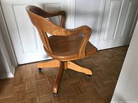 Side view of the solid oak office chair showing the curved armrest, vertical slat back, and wheeled base.