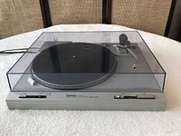 Front angled view of Technics SL-202 turntable with clear dust cover closed, showing buttons and switches, placed on table.