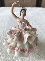 Front view showing classic dancer pose, detailed facial features, textured dress with pink trim and flower in hand