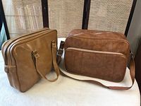Photo showing both vintage carry-on bags side by side on a white surface with a chair behind them.