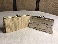 Two vintage clutch purses displayed side by side on a light surface with wood background. One clutch is cream colored with beaded design and a chain strap, the other is floral fabric with gold frame and clasp.