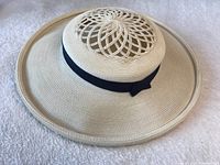 Front angle view of the vintage light-colored woven straw hat showing the wide brim, circular open weave crown pattern, and black ribbon band with bow detail.