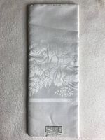 Folded vintage white linen tablecloth showing woven floral pattern detail.