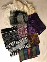 Full assortment of nine vintage shawls laid out showing variety of colors and patterns including solids, stripes, and florals.