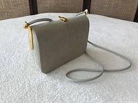 Side view of light grey suede purse showing rectangular shape with gold-tone clasp and single shoulder strap.