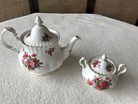 Tea pot and sugar bowl on table, showing full view and floral pattern.