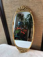 Front view of vintage wall mirror with gold floral frame and rose decorations showing indoor plants reflected