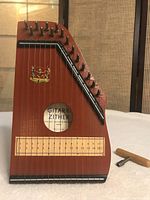 Close-up of wooden Gitarr Zither musical instrument showing tuning pins, strings, decorative emblem, and tuning key nearby.