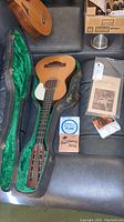 Ukulele, hardshell case open with green interior, book and string packs