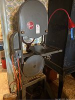 Full view of gray Delta band saw with table and red electrical cord attached, showing the saw's frame and wheels.