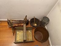 Wide view showing brass firewood basket, bucket, coal scuttle with ladle, iron fire poker, and brass and iron andirons against a corner of the room.