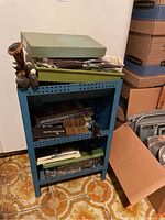 View of blue shelf unit holding boxes and cutlery stand with Hanford Forge cutlery and Oneida flatware boxes on the top shelf.