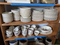Wide view of shelf with stacks of various plates, bowls, and tea mugs all with floral pattern.