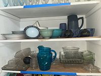 Shelf with various glassware, ceramic pitchers, serving bowls and baking dishes showing overall lot contents.