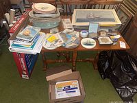 Overview of table showing plates, trays, books, prints, coins and postcards