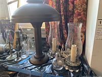 Image showing the vintage standing lamp with dome-style metal shade and the glass hurricane lamps with candle-like structures inside on a plastic covered table.