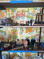 Shelf view showing pipes, pocket watch case, candlesticks, lighter and various small items