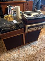 Photo showing full stereo setup including the turntable with clear acrylic dust cover on the left, large speakers below, and the cassette deck and stereo amplifier stacked on the right.