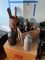 Wide view showing leather case, powder flask body, Pepsi crate, sextants and thermos on cardboard box