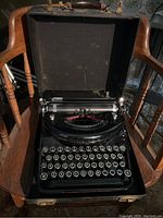 Black Underwood Noiseless portable typewriter in black carrying case resting on wooden chair, showing full keyboard and ribbon mechanism.
