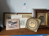 Overview of seven varied wall art pieces including prints, framed pictures, and metal plaque arranged on wooden surface