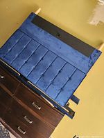 Blue velvet tufted headboard and frame laid on top of a dresser showing front fabric details and black backing