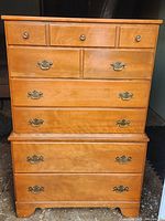 Front view of mid-century modern Ethan Allen highboy chest with multiple drawers and brass handles.