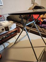 Side view showing table legs and part of black round top, illustrating foldable structure.