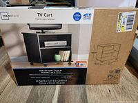 Photo of the Mainstays TV Cart in its original packaging showing front and side views, box with product image, specifications and assembly information.