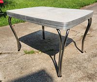 Rectangular table with light-colored Formica top and curved metal legs, missing one leg cap.