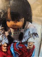 Close-up of doll's face and upper body showing traditional dress with fringe and bead decoration.