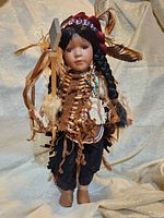 Full view of the Native American porcelain doll with traditional clothing, braided hair, bead necklaces, and feathers.
