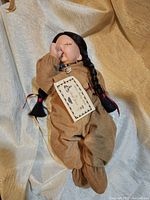 Full view of the porcelain Native American doll with black braided hair and brown outfit.