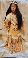Full view of Native American porcelain doll in traditional attire showing dress, beadwork and hair.