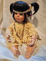 Full front view of the Native American porcelain doll sitting with pigtails and traditional clothing.