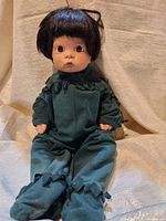 Full front view of the porcelain doll seated, showing the green one-piece outfit with ruffles and black hair.
