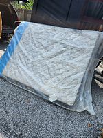 Mattress in plastic packaging outdoors showing quilted beige top and blue border