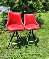 Pair of red vinyl mid-century modern barstools with black metal bases, shown outdoors on grass.