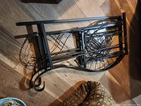 Side view of the metal plant stand laid flat on the floor showing curved metal sides and structural bars with three circular tiers.