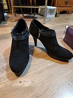 Front and side view of black suede high heel ankle shoes with strap and zipper.