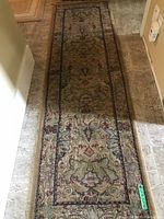 Photo of the entire length of the Oriental style runner rug laid out in a hallway on tile flooring showing pattern and wear.