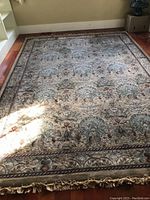 Full view of the area rug laid out on wooden floor showing the floral and leaf patterned design in muted colors with fringed edges.