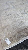 Shows full view of the Jordans area rug laid out with visible fringed edge and tag with measurements.