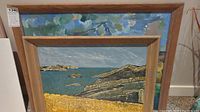 Two framed paintings leaning against wall, seascape visible in front