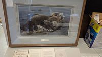 Frontal view of the framed artwork showing two sea otters on water.