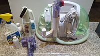 Photo overview of entire lot showing the Bissell Little Green carpet cleaner unit with hose and attachments, multiple cleaning bottles, and spray bottles for cleaning solutions.
