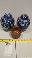 Two blue and white ceramic ginger jars with floral patterns alongside a small wooden bowl, all measured with a ruler for scale.