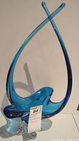 Full view of the blue handblown glass sculpture showing its height and curving design with clear glass feet.