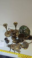 Photo showing brass items including two candlesticks, stained glass lamp shade, boot-shaped candle holder, bird-shaped candle holder, and a small container.